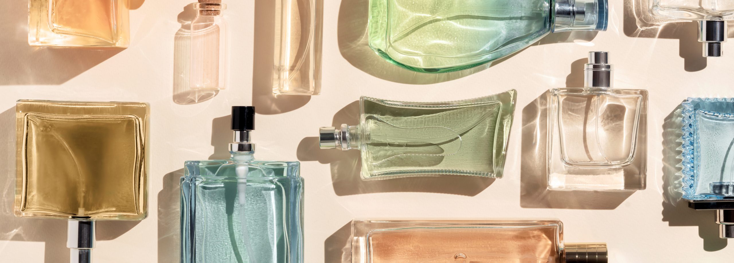 perfume bottles. a lot of transparent multicolored glass bottles of cosmetics, on a beige background. art composition flat lay panoramic.