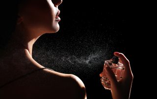 Woman spraying luxury perfume on black background, closeup