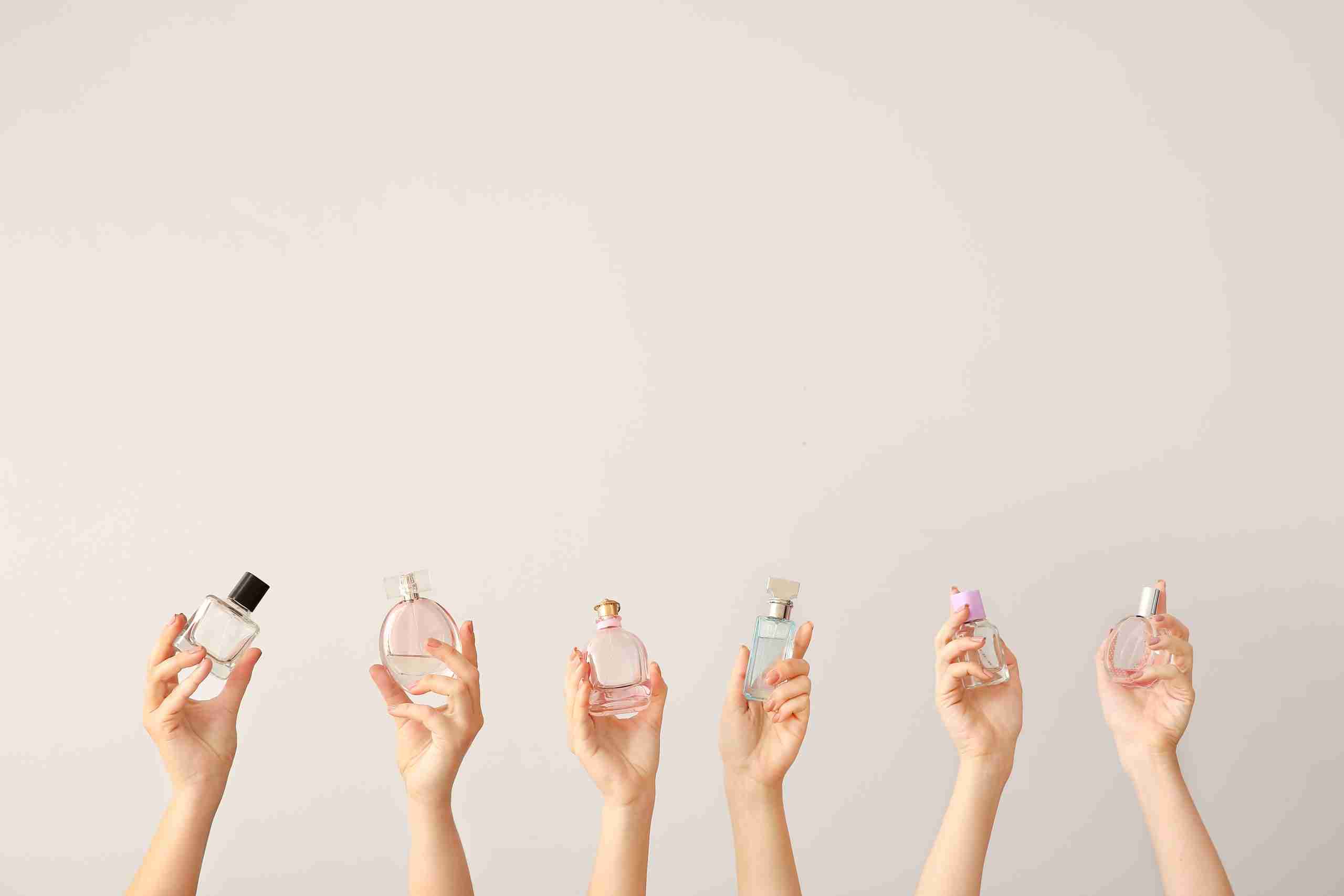 Female hands with different perfume bottles on grey background