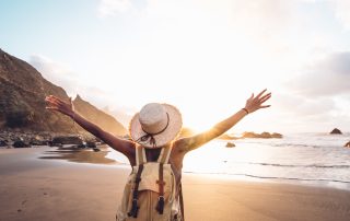 Happy woman with arms up enjoy freedom at the beach at sunset. Wellness, success, freedom and travel concept - perfumes for every type of vacation