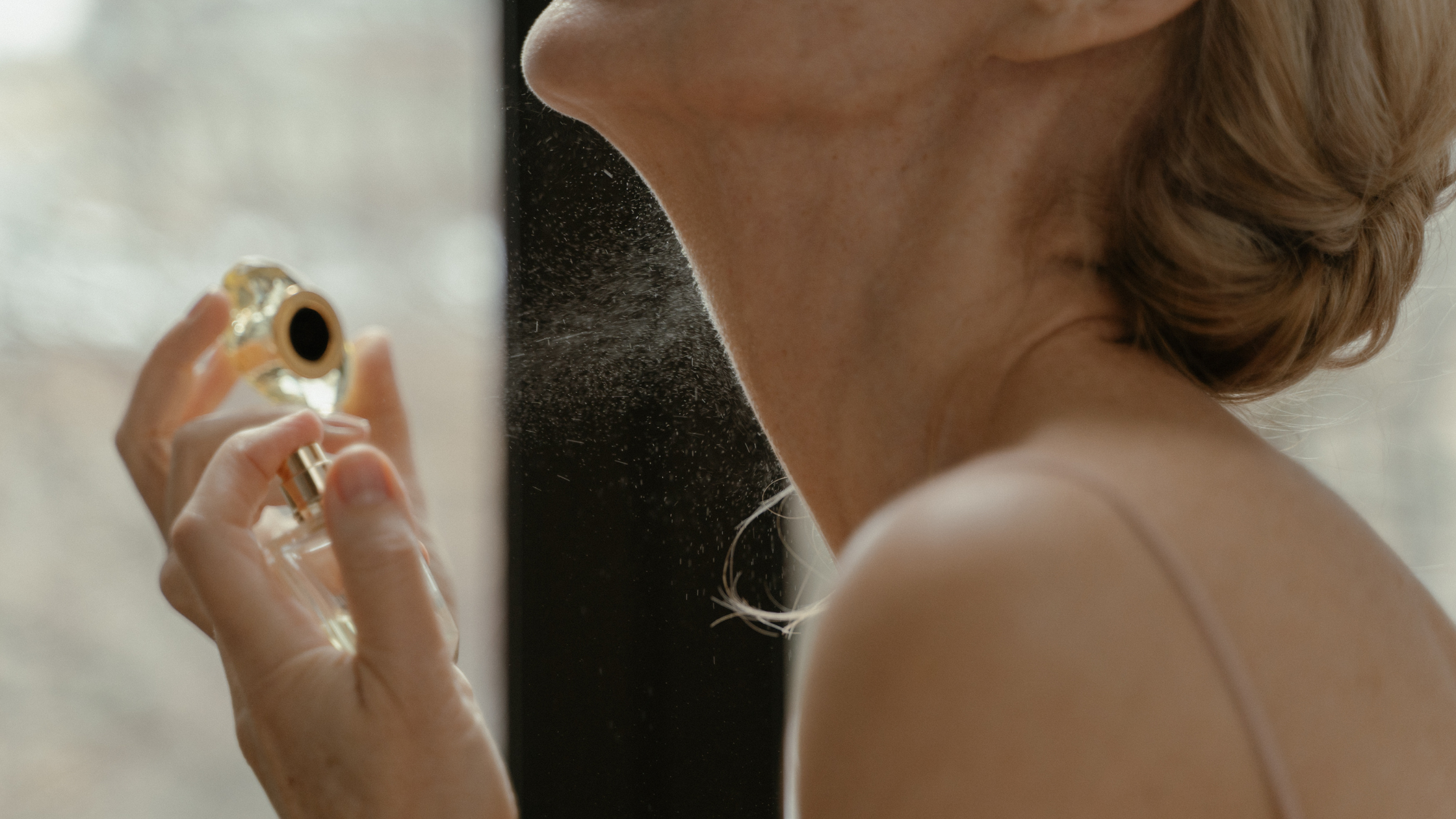 Woman spraying perfume on her neck - closeup