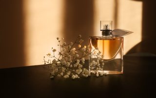Transparent bottle of perfume with beautiful flowers on dark table