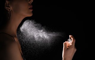 Woman spraying luxury perfume on black background, closeup
