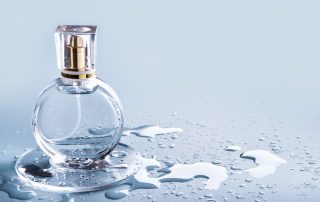 Glass perfume bottle and rain drops on blue background.