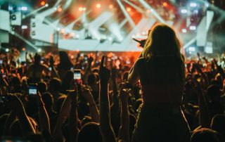Stage lights against woman with with arms raised while enjoying a concert on a music festival. Crowd with raised hands.