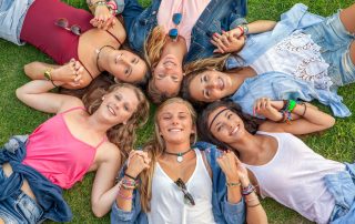 smiling teen girls lying on the grass in a circle holding hands